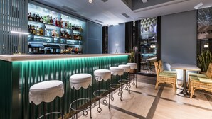 A bar area with a green bar counter, striped stools, and a seating area with wicker chairs and a table. - Intelier Casa de Indias Hotel by Intelier Hotels & Suites (Seville)