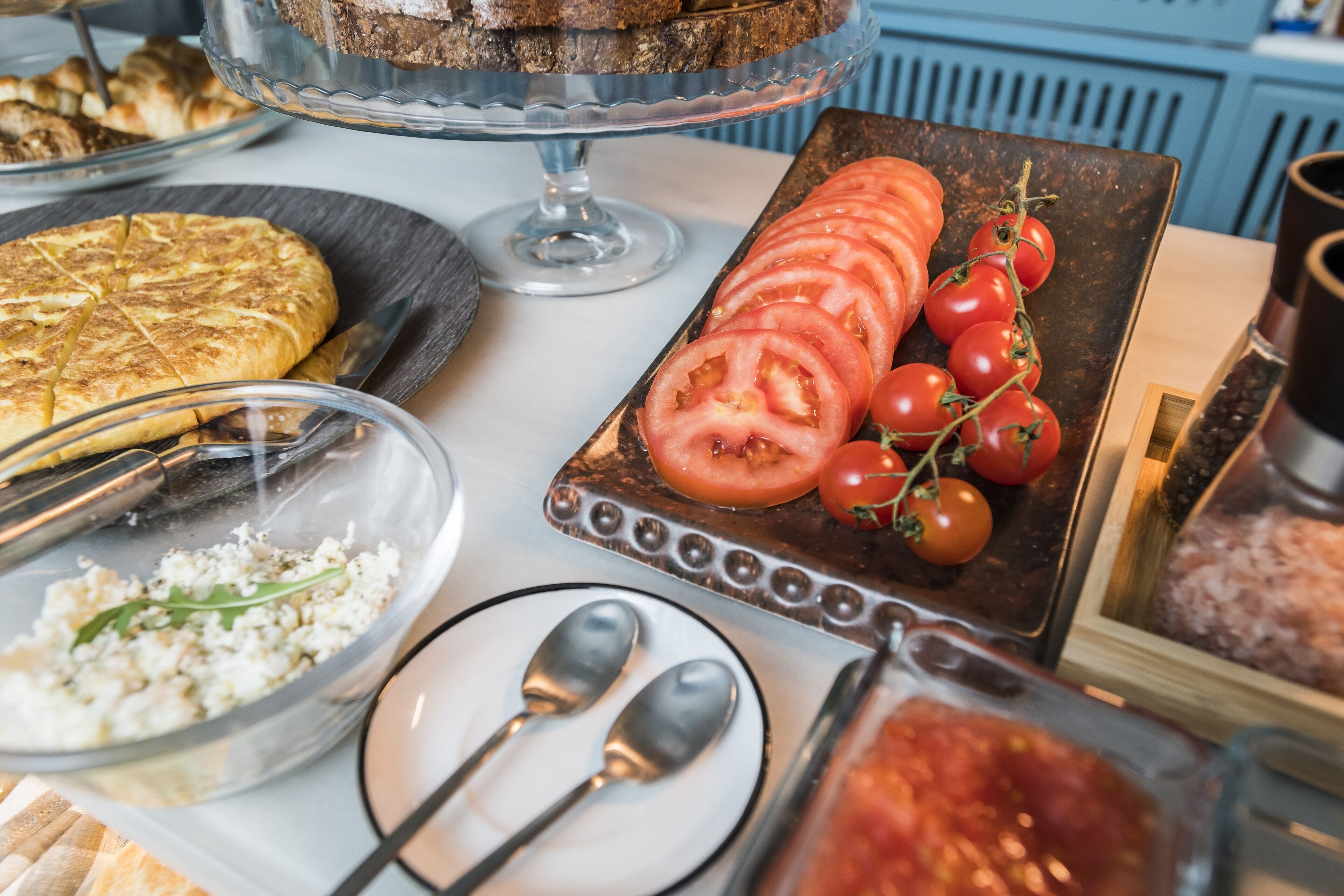 Una mesa de buffet con diversos alimentos, incluyendo una quiche, tomates en rodajas y un bol de ensalada.