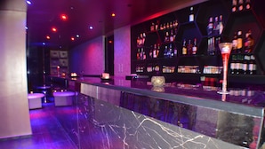 Una zona de bar con mostrador de mármol, estantes llenos de botellas y un vaso decorativo.