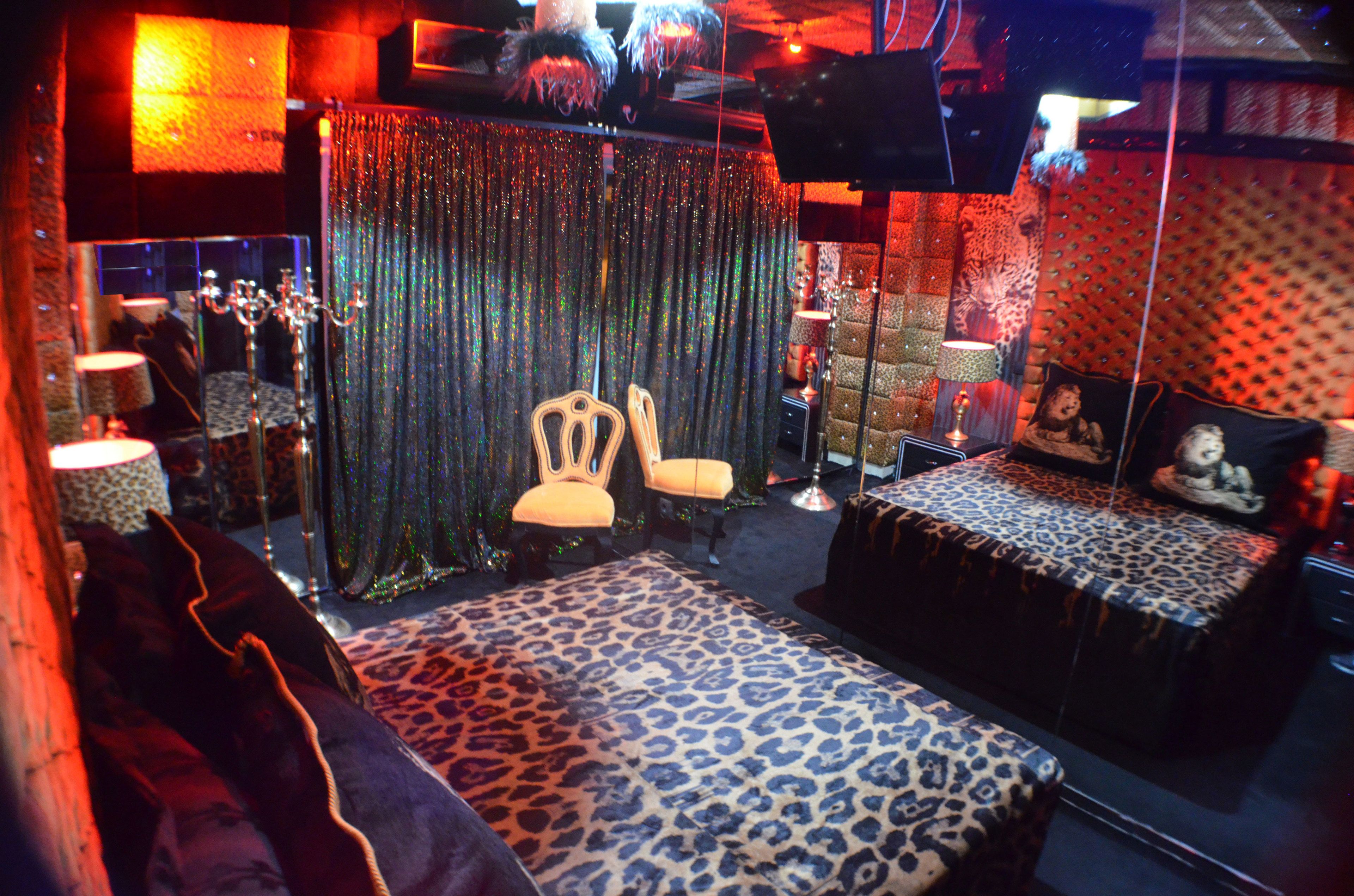Una habitación con alfombra de estampado de leopardo, una cama con colcha estampada, una silla y un espejo que refleja la habitación.