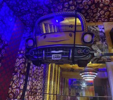 Un coche clásico suspendido en una habitación con papel tapiz estampado y una araña.
