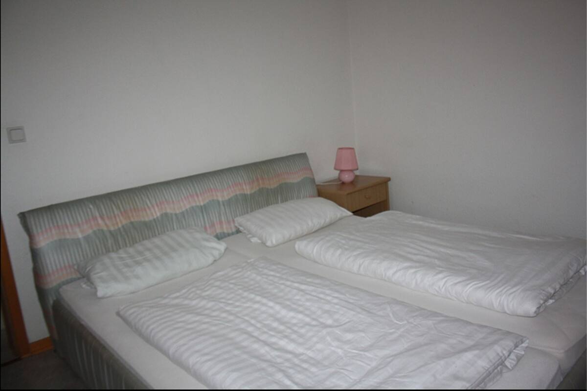A double bed with white linens, a striped headboard, and a pink bedside lamp.