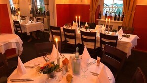 A restaurant with round tables set for dining, candles, and a vase with flowers. - Hotel Anker (Linden)