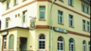 A multi-story building with a yellow facade, multiple windows, and a street sign. - Hotel Anker (Linden)
