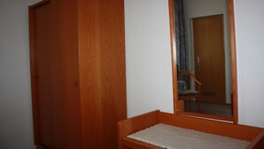 A room with a wooden wardrobe, a small wooden bench, and a mirror reflecting a door and a chair. - Hotel Anker (Linden)