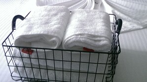 Una cama bien tendida con sábanas blancas y un perchero metálico lleno de toallas dobladas.