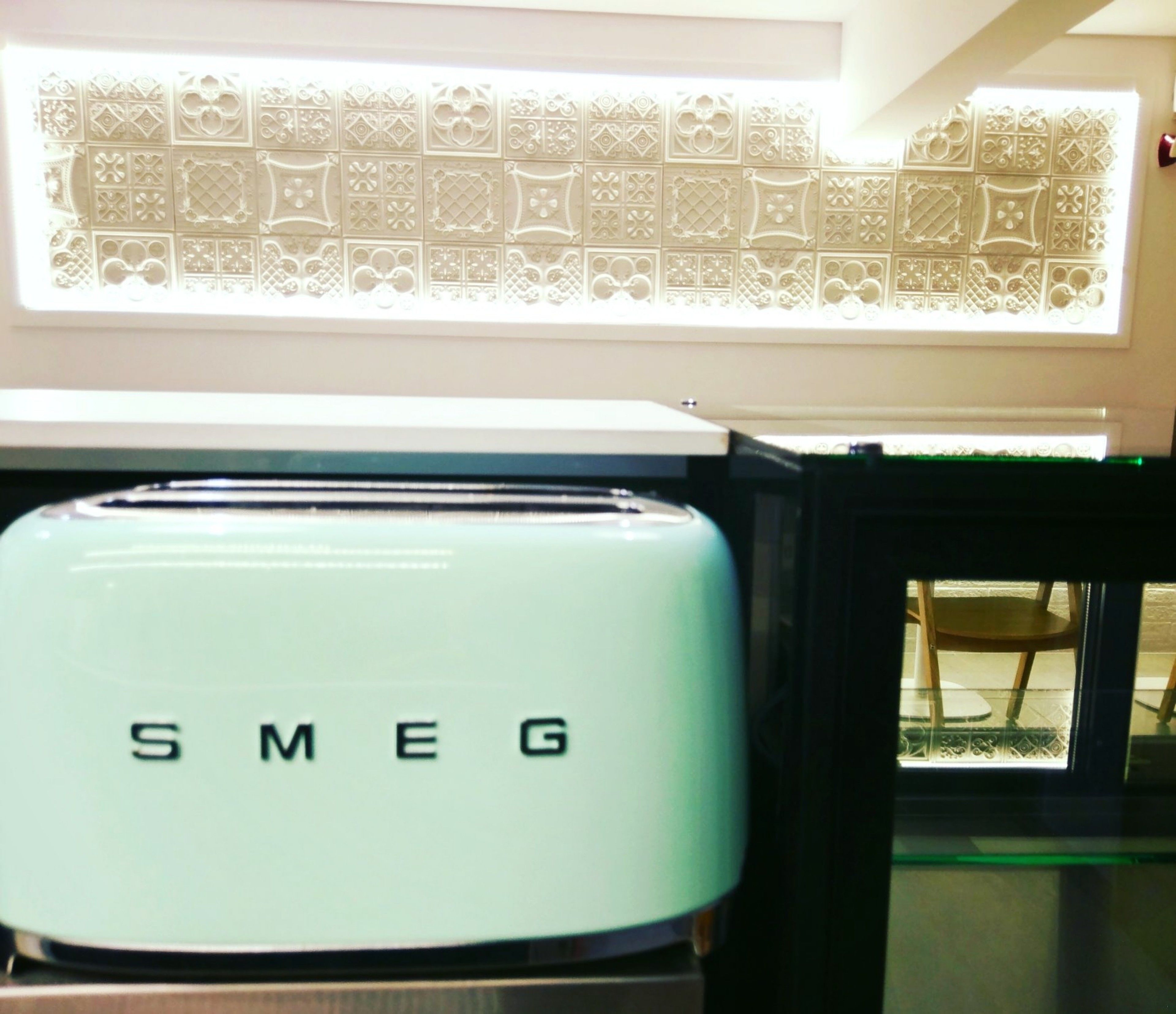 Un electrodoméstico Smeg azul claro en una cocina con azulejos decorativos.