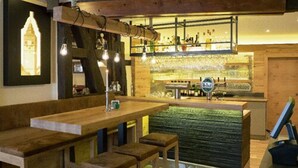 A bar area with wooden stools, a counter, and hanging light fixtures. - Hotel Schneider (Lich)