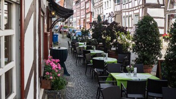 A narrow cobblestone street with outdoor seating, traditional half-timbered buildings, and potted plants. - Hotel Schneider (Lich)