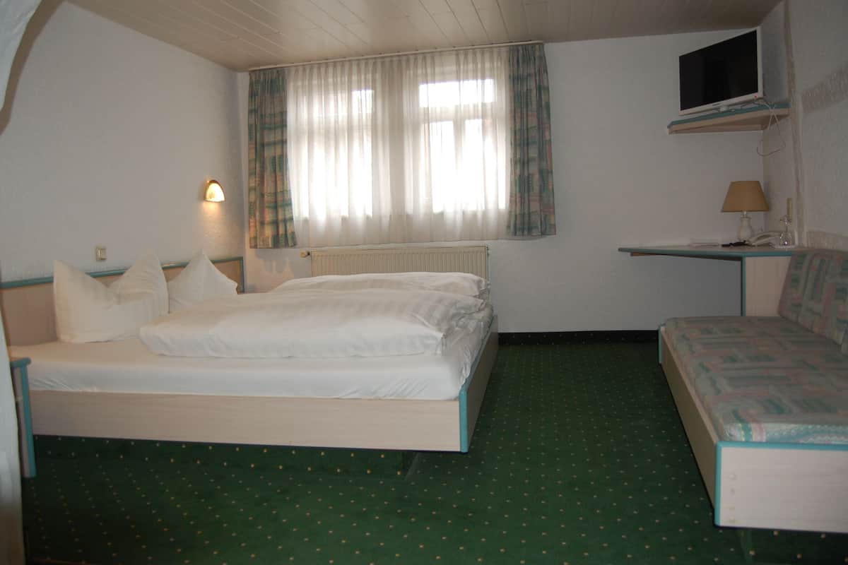 A room with a bed, a desk, a chair, a television, and a window with curtains.