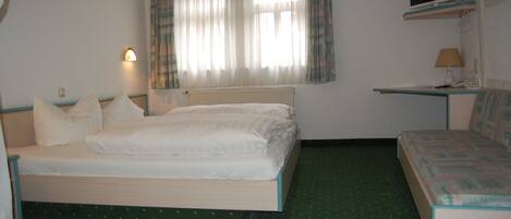 A room with a bed, a desk, a chair, a television, and a window with curtains.