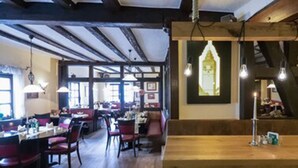 A restaurant interior with wooden beams, hanging light bulbs, and a large framed picture on the wall. - Hotel Schneider (Lich)