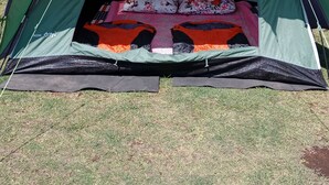 Une tente est installée sur l’herbe, et on peut voir une maison et des collines au loin.