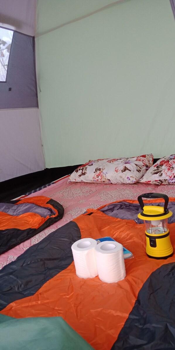 A tent interior with a bed, pillows, a lantern, and two rolls of toilet paper.