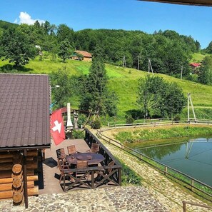 Una cabaña de madera con una bandera suiza, un patio de piedra y vistas a un estanque y colinas verdes.