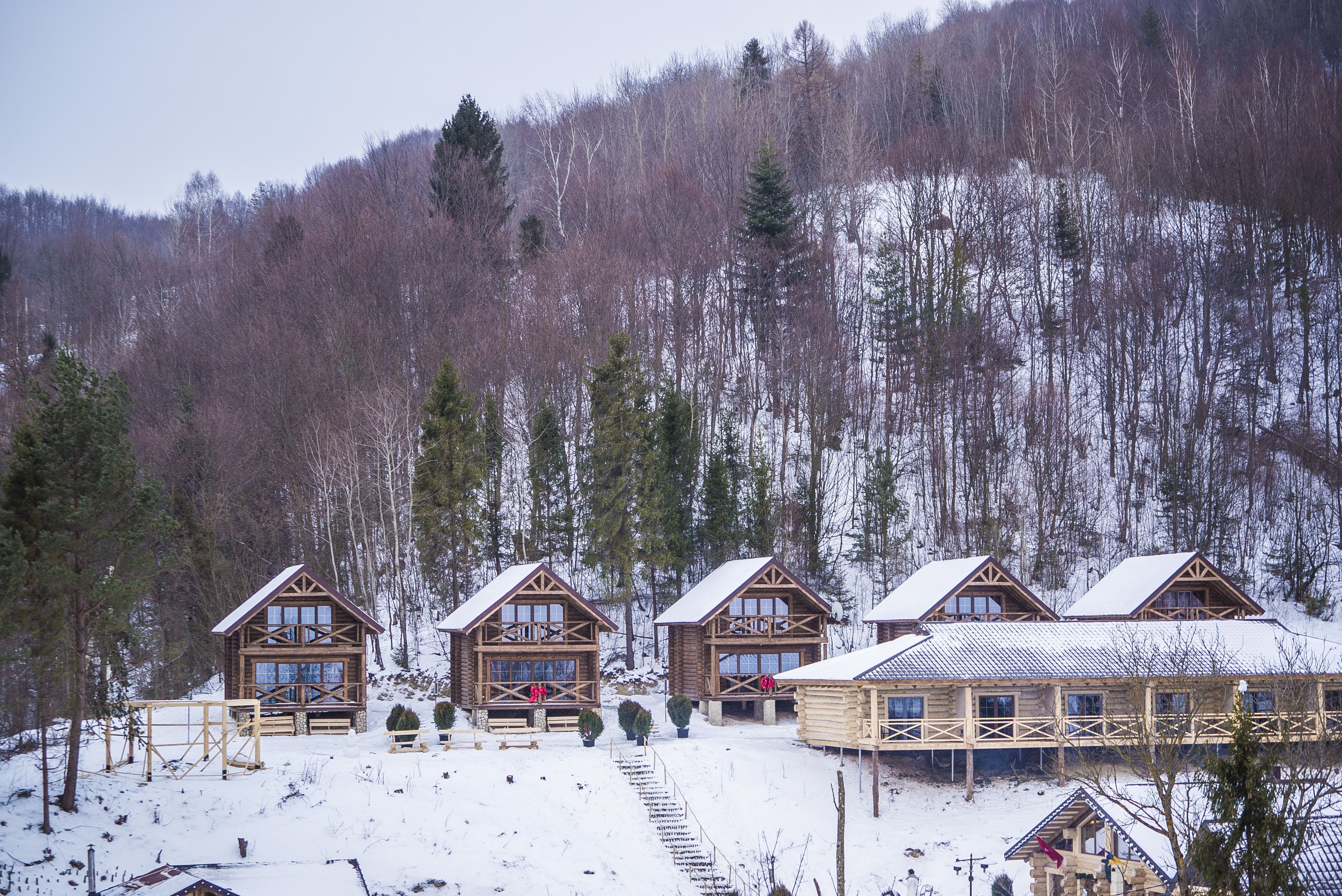 A row of log cabins with a wooden deck and a ski lift in the background.