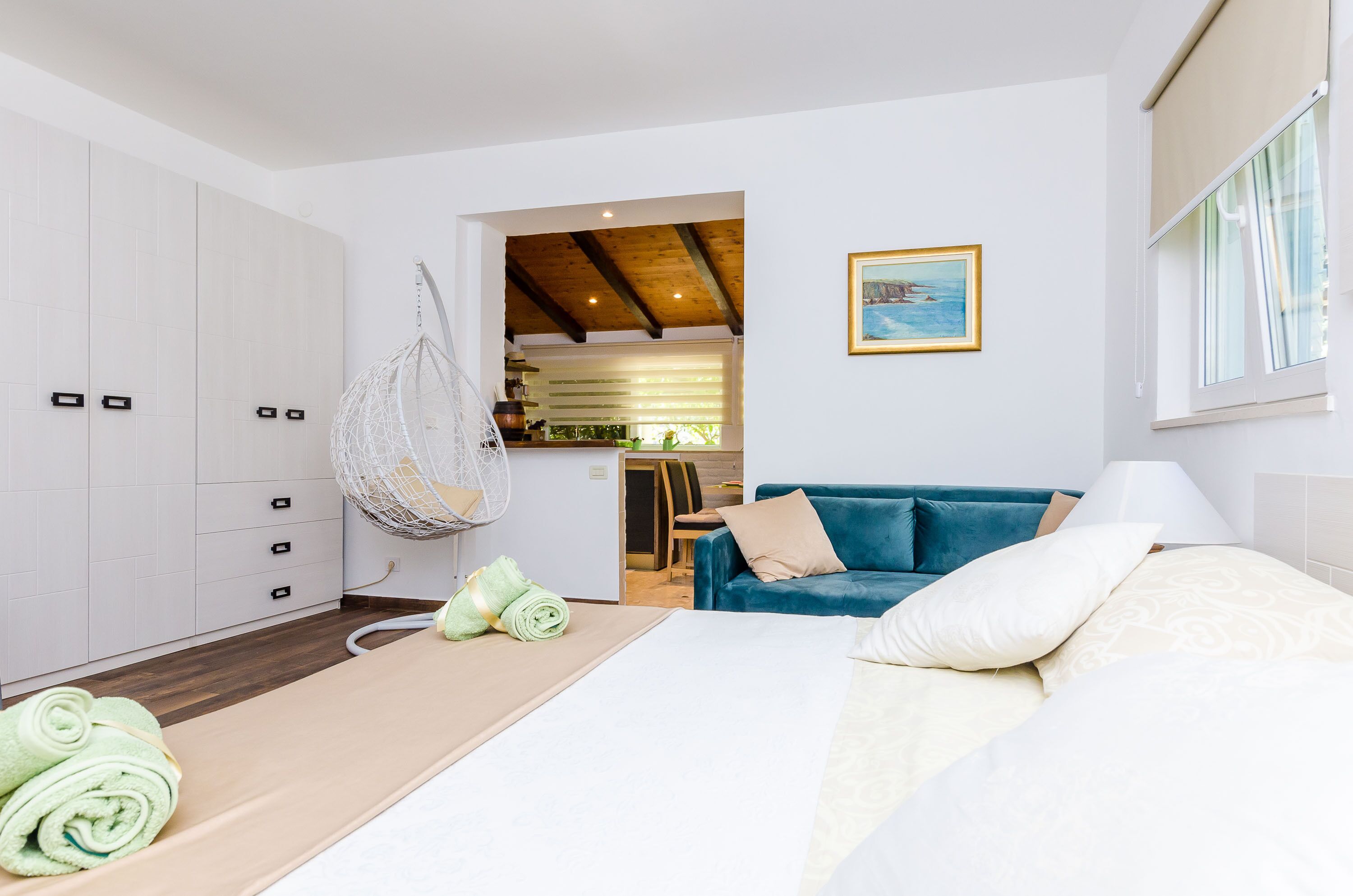 A modern bedroom with a bed, a hanging chair, a sofa, and a view of the kitchen.