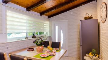 A dining area with a wooden table, chairs, a potted plant, and a clock on the wall.
