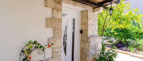 A stone-walled entrance with a white door, a metal gate, and a potted plant.