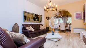 Un soggiorno moderno con un divano marrone scuro, un tavolino bianco, una poltrona sospesa e un lampadario.