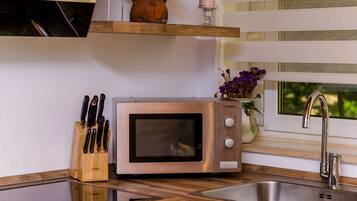A kitchen with a stainless steel microwave, a knife block, a vase with flowers, and a window with a view of greenery.