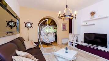A modern living room with a brown sofa, a white coffee table, a TV, a chandelier, and a hanging chair.