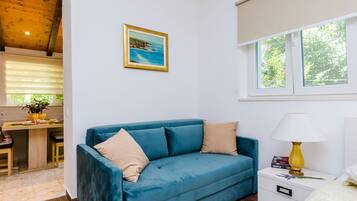 Een moderne woonkamer met een blauwe bank, een klein wit nachtkastje met een lamp, en een schilderij van een kustlandschap.