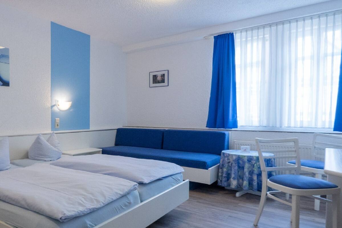 A hotel room with a bed, a seating area, a desk, and a window with curtains.