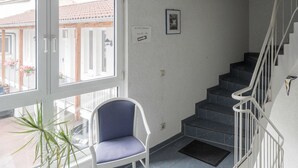A staircase with a chair and a potted plant in a room with a view of buildings outside. - Hotel Holländischer Hof (Lich)