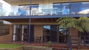 A modern building with a glass balcony, outdoor seating, and a small garden area. - Spacious, comfortable, family home. Great views, pets ok, free wifi (Lakes Entrance)
