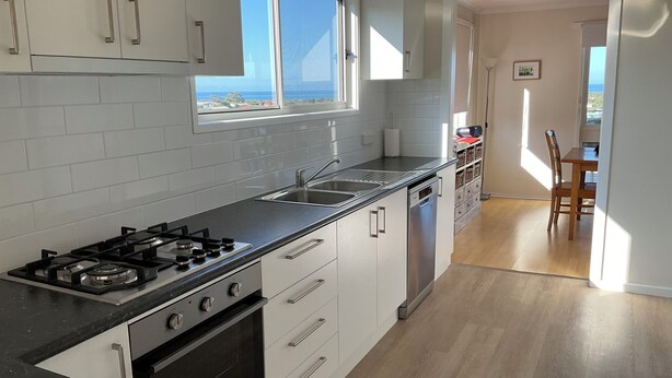 A modern kitchen with white cabinets, a black countertop, a built-in oven, and a dishwasher. There is a window providing a view of the outdoors. - Spacious, comfortable, family home. Great views, pets ok, free wifi (Lakes Entrance)