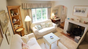 A cozy living room with a sofa, a small table, a bookshelf, and a fireplace. - The Mews Cottage (Salisbury)