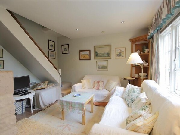 A cozy living room with a sofa, a small table, and a lamp. There is a staircase leading to another level. - The Mews Cottage (Salisbury)