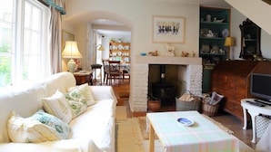 A cozy living room with a fireplace, a sofa, a dining table, and a television. - The Mews Cottage (Salisbury)