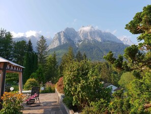 A garden with a bench and a gazebo, surrounded by trees and a mountain view. - Alpenchalet Zum-Jeremia (Grainau)
