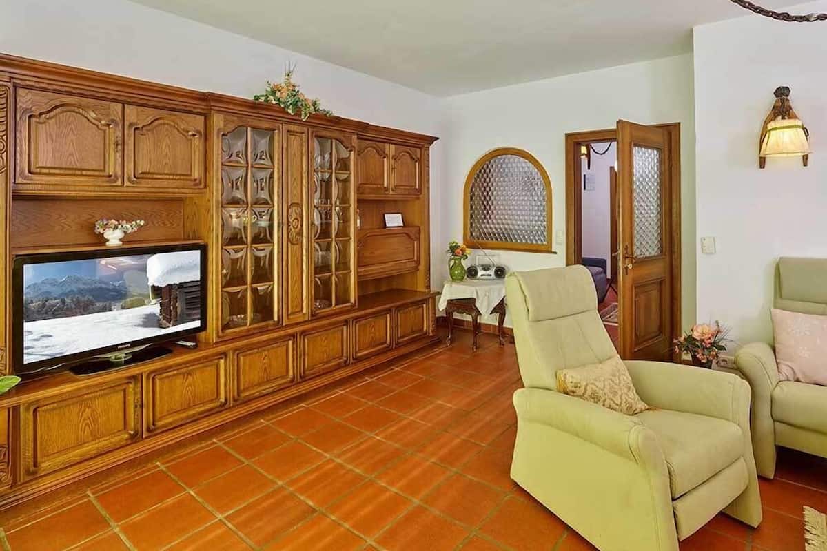 Ein Wohnzimmer mit Fernseher, Holzschrank und zwei Sesseln.