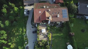 Vista aérea de una casa con techo inclinado, varias ventanas y un camino de entrada con coches estacionados.