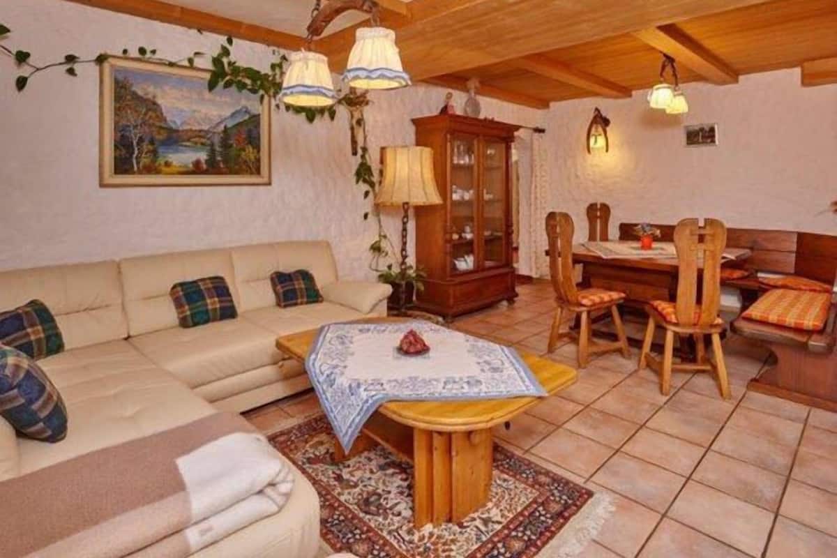 Ein gemütliches Wohnzimmer mit einer Couch, einem Esstisch und Stühlen. An der Wand befinden sich ein Schrank und ein Gemälde.