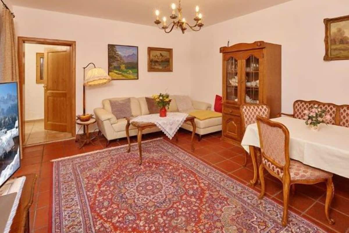 Ein gemütliches Wohnzimmer mit einer Couch, einem Esstisch mit Stühlen, einem Schrank und einer Deckenleuchte.