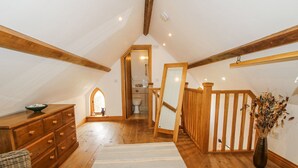 A spacious attic room with wooden beams, a large mirror, a wooden dresser, and a striped rug. - The Shooting Folly (Market Drayton)