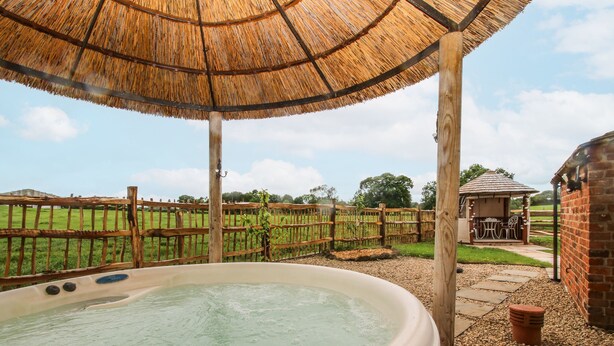 A hot tub under a thatched roof, surrounded by a wooden fence and a brick wall. - The Shooting Folly (Market Drayton)