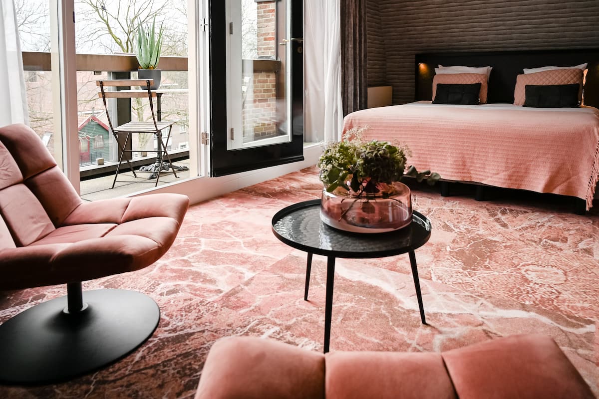Ein modernes Schlafzimmer mit einem großen Bett, einer Topfpflanze auf einem kleinen Tisch und Blick durch eine Glastür nach draußen.