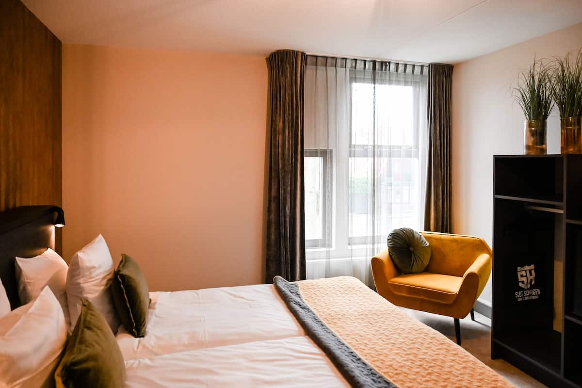 Ein Hotelzimmer mit einem Bett, einer Couch, einem Fernsehmöbel und einem Fenster mit Vorhängen.