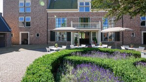 A multi-story brick building with a balcony, outdoor seating area with tables and chairs, and a landscaped garden with purple flowers. - Fletcher Slothotel Schagen (Schagen)