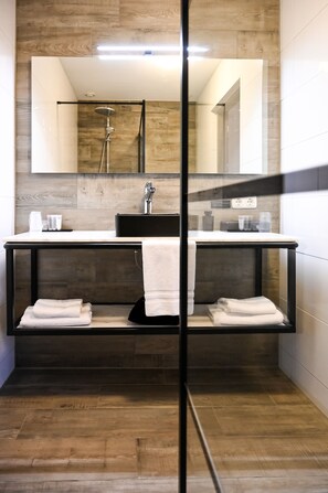 Une salle de bain moderne avec un plancher en bois, un meuble-lavabo noir avec un miroir et un espace douche.