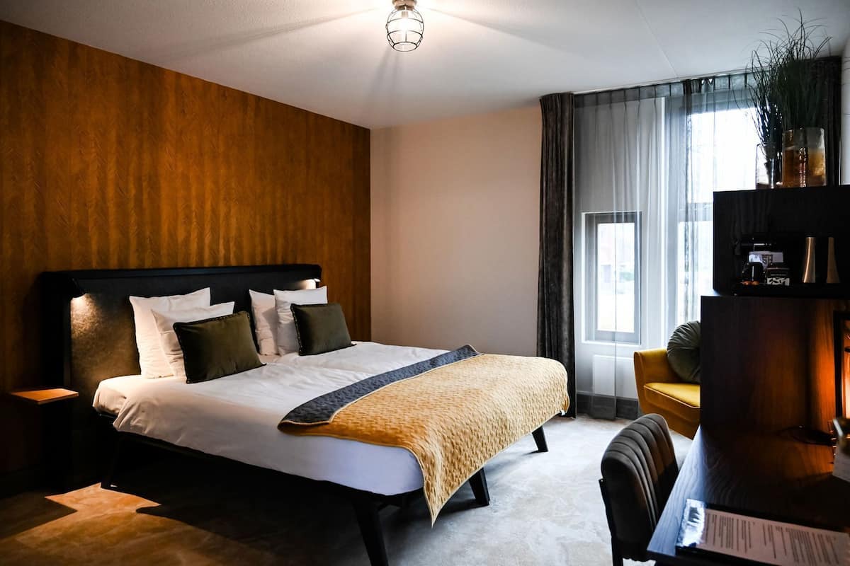 Ein Hotelzimmer mit Bett, Nachttischen, Schreibtisch, Stuhl, Bücherregal und einem Fenster mit Vorhängen.
