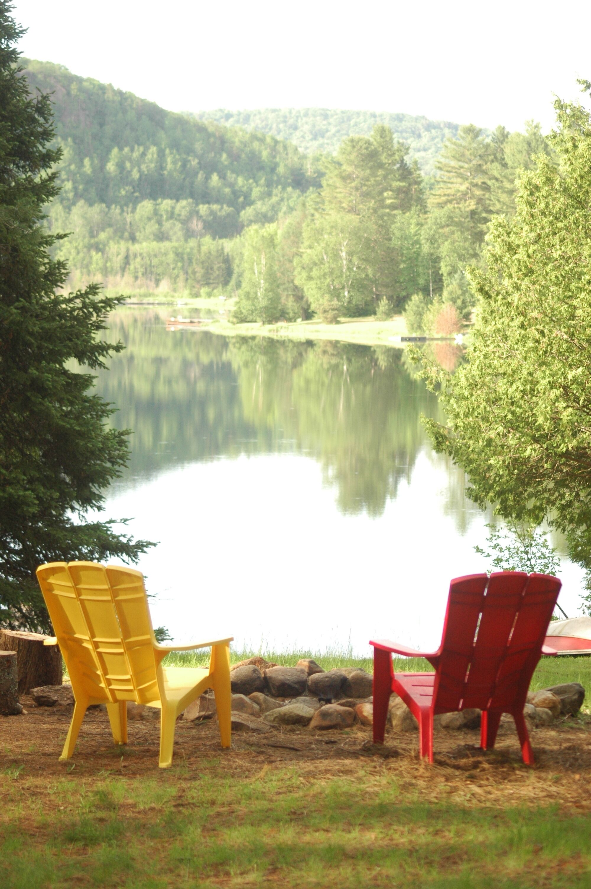 Two Adirondack chairs facing a calm lake with a forested hill in the background.