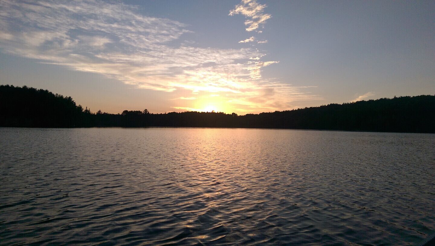 A calm lake at sunset with a forested shoreline.
