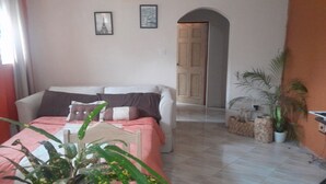 Une chambre à coucher comprenant un lit, un canapé, une plante en pot et une porte donnant sur une autre pièce.