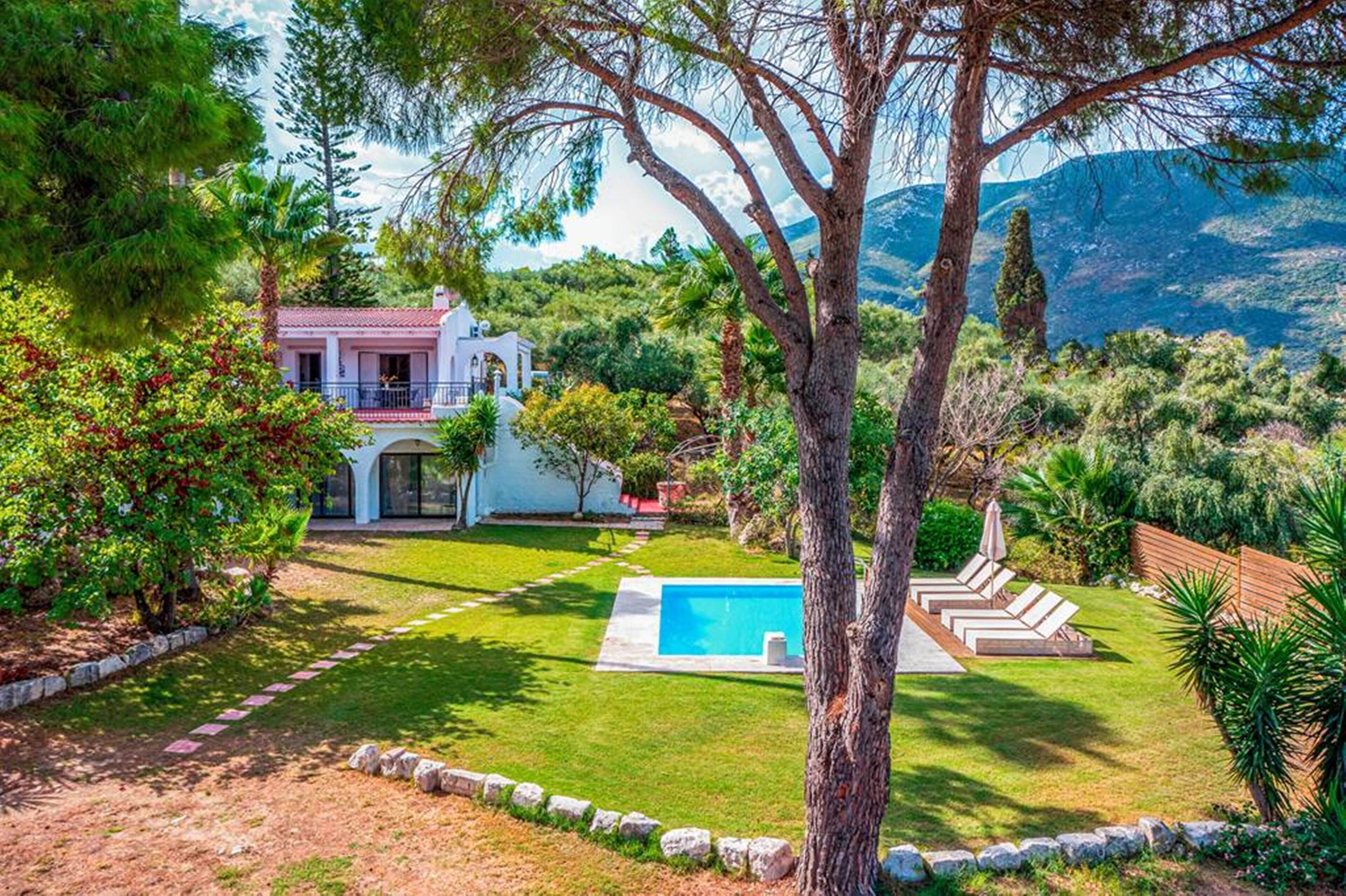 A house with a swimming pool, surrounded by a well-maintained lawn and trees.